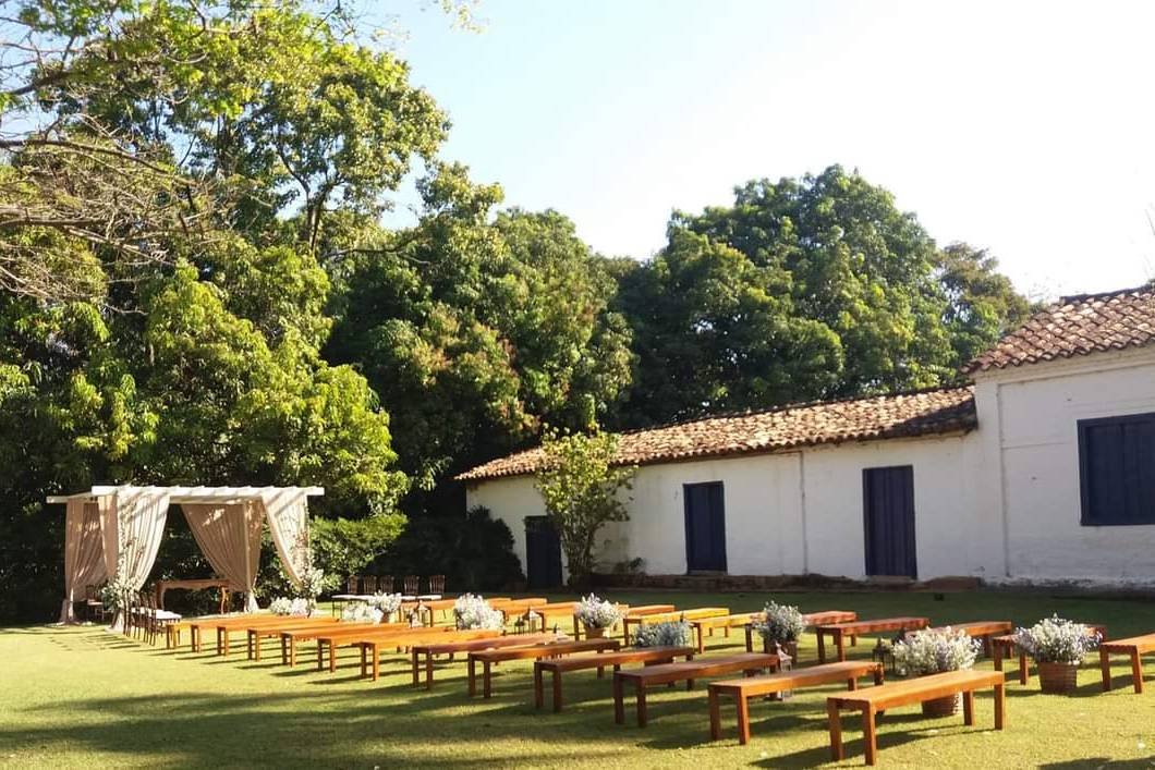 Bancos de madeira e altar de cortinas montados no gramado diante da casa