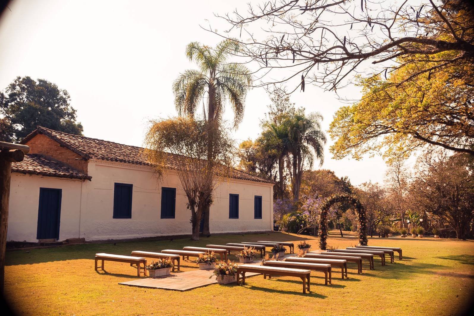 A fachada ao fim da tarde, com a palmeira, os bancos da cerimônia e o arco de flores no gramado