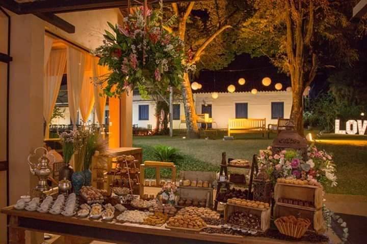 Mesa de doces à noite, com a casa iluminada ao fundo