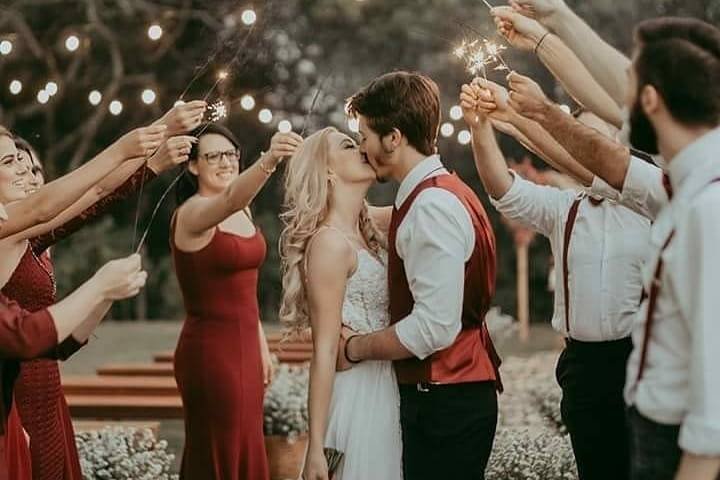 Beijo dos noivos sob os braços erguidos dos padrinhos com faíscas acesas