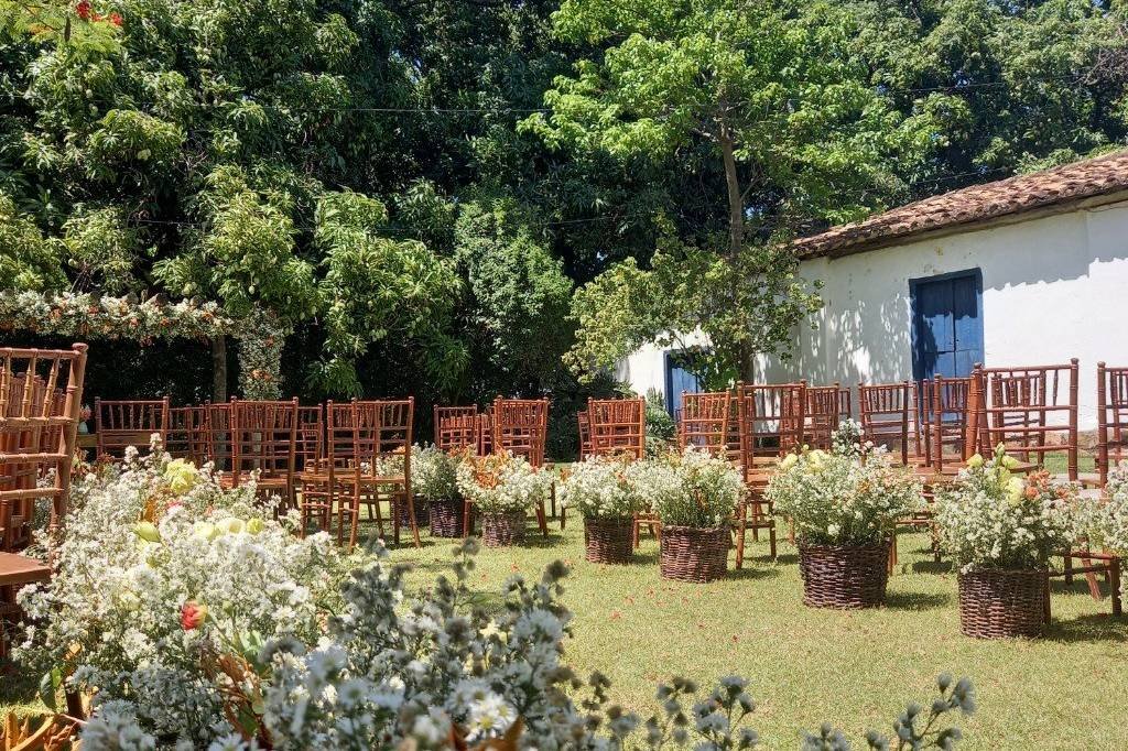Cadeiras de madeira e cestos de flores prontos ao lado da casa, esperando os convidados