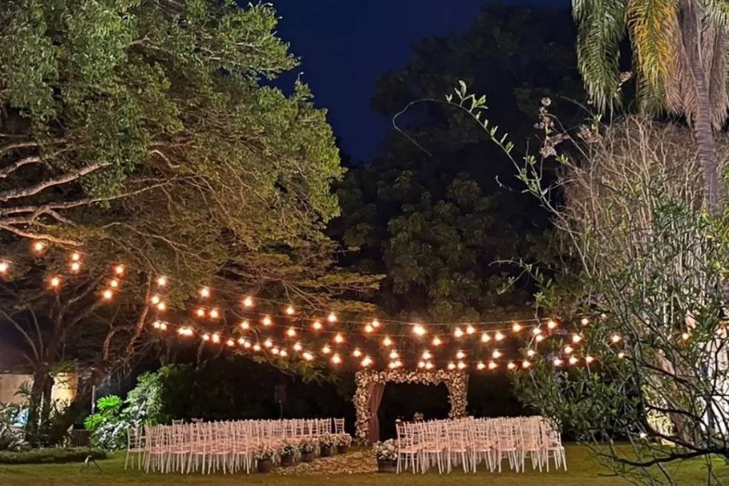 Cerimônia montada no jardim à noite, sob varais de lâmpadas entre as árvores