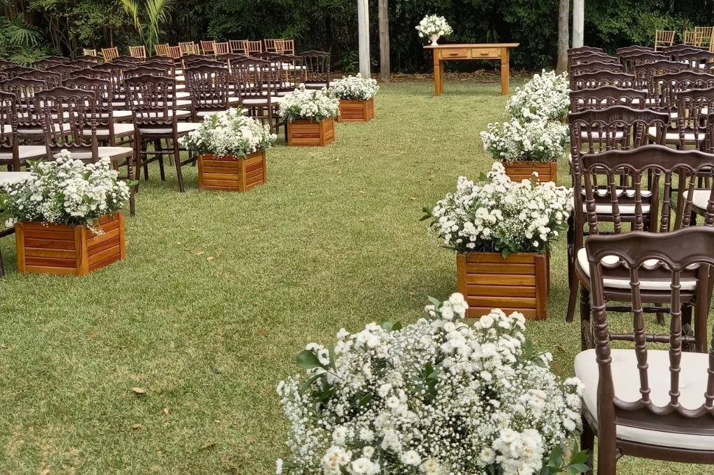 Cadeiras de madeira e arranjos de flores brancas em caixotes ao longo do corredor